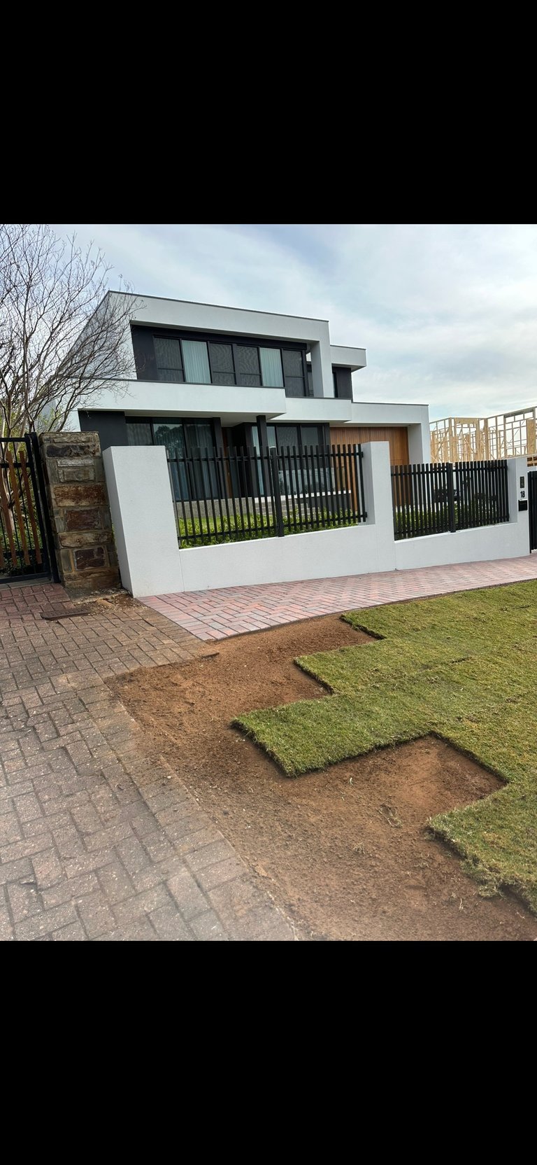 Modern white and black two-story house with horizontal fencing, brick patio, and patchy lawn in front yard