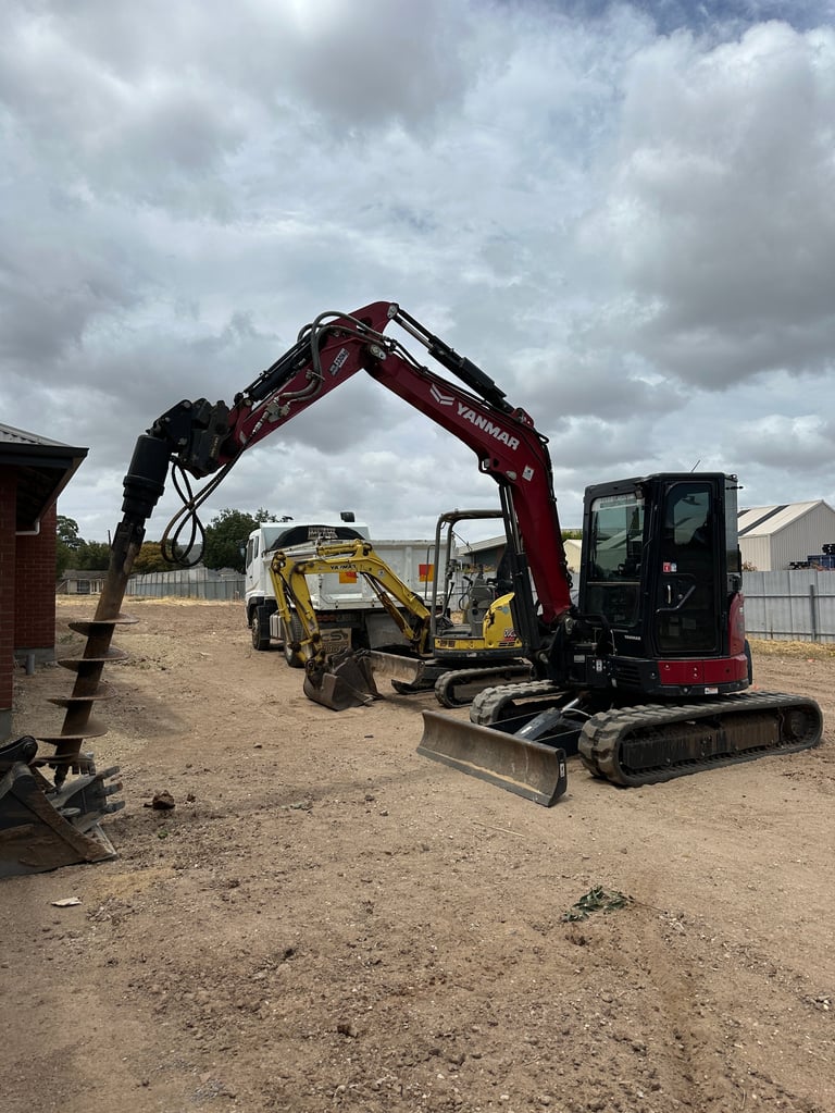 Red mini excavator with extended arm on construction site next to yellow skid steer loader on sandy ground