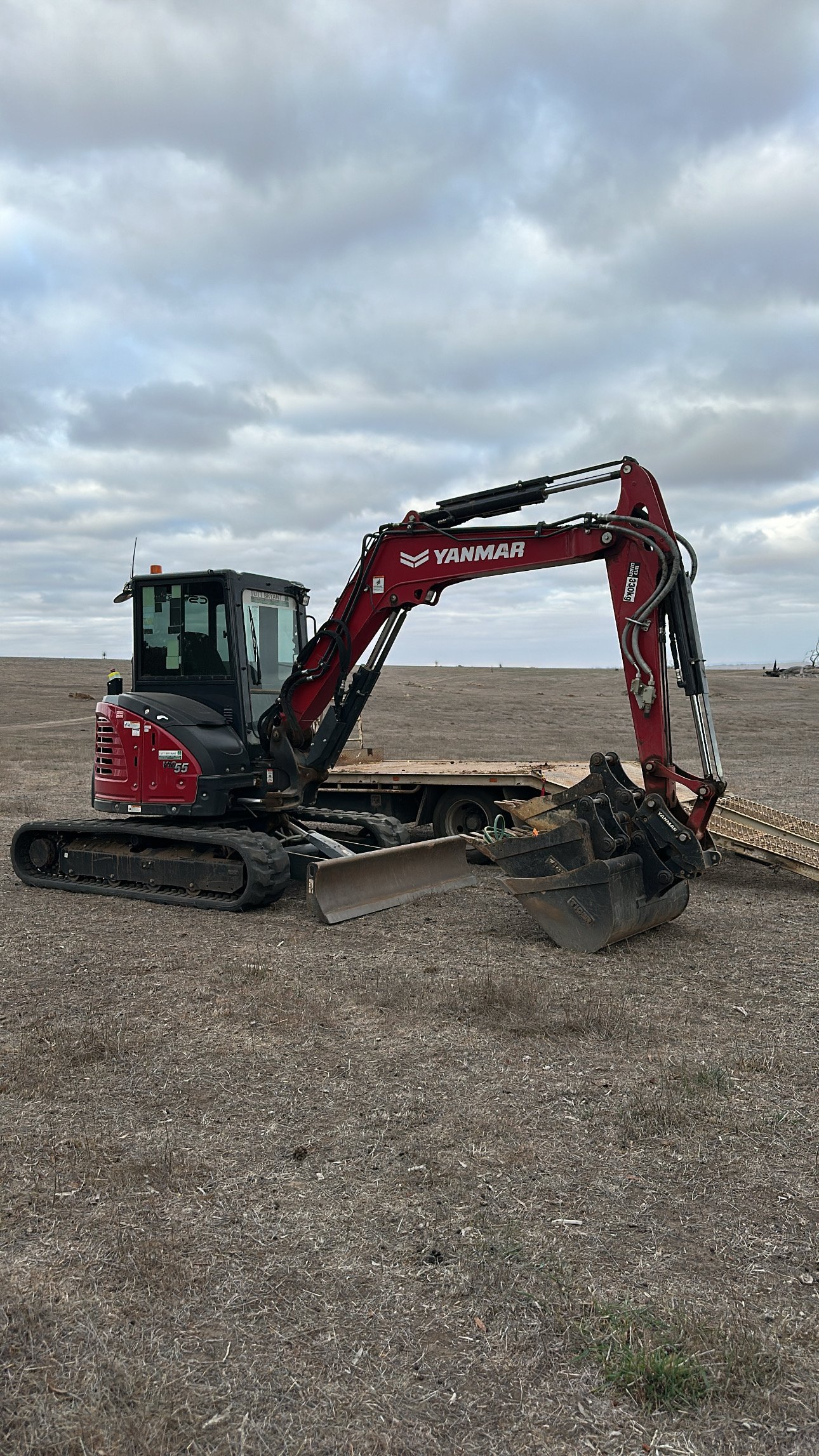 Red Yanmar compact excavator on barren field with articulated arm and bucket under cloudy sky