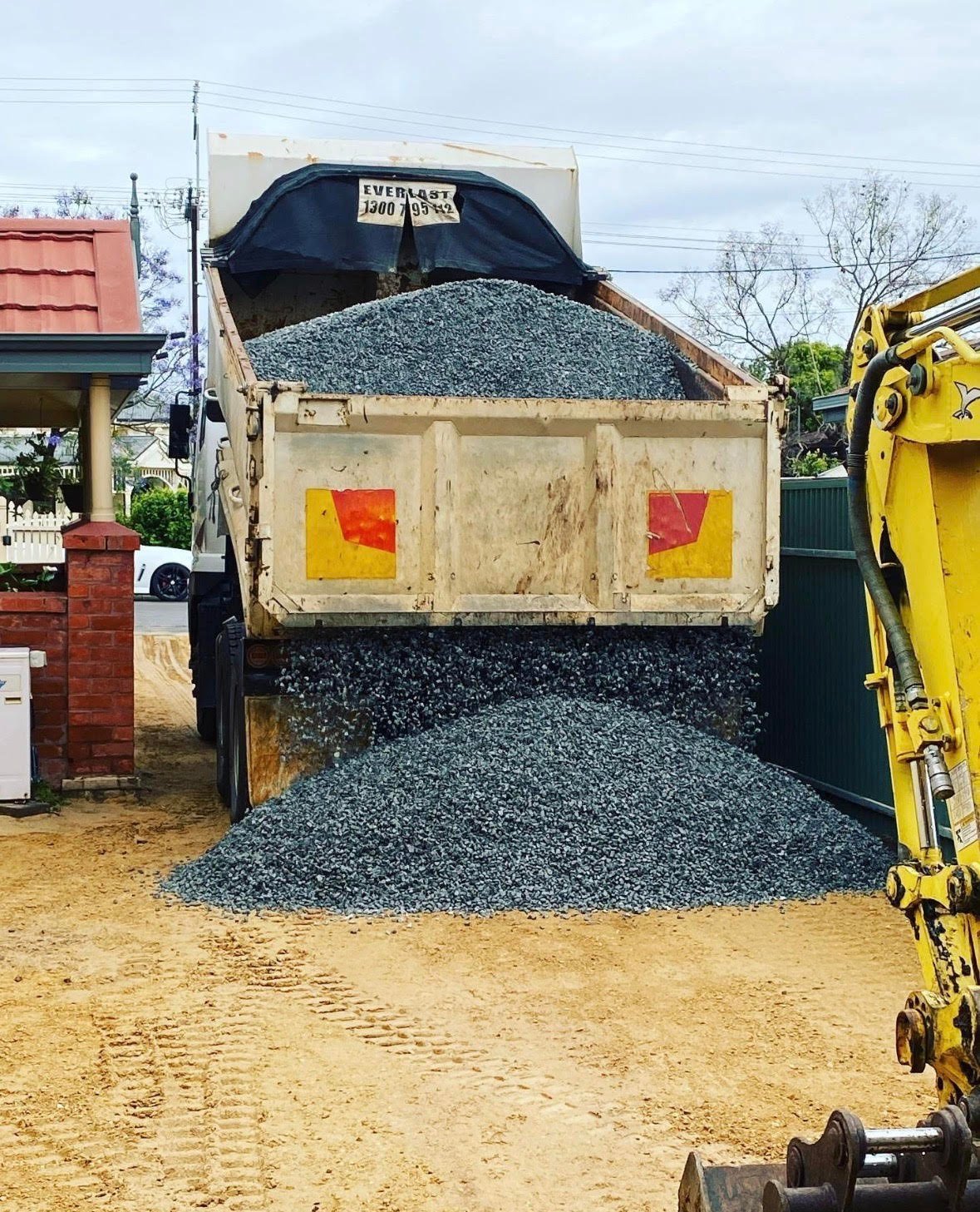Dump truck loaded with gravel unloading at construction site with yellow excavator nearby