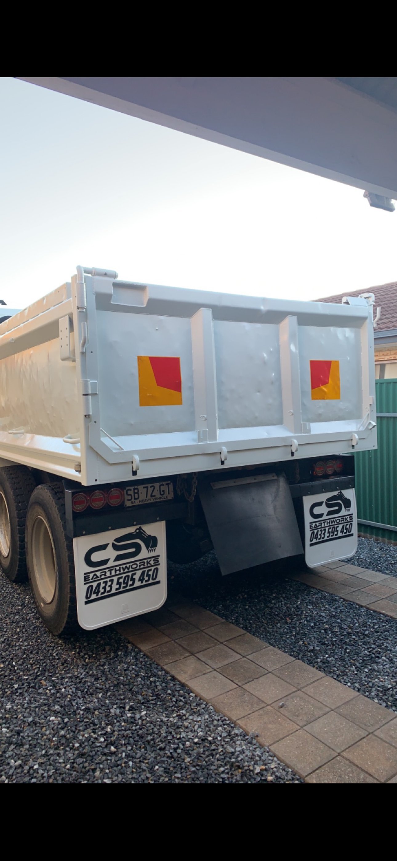 Rear view of a gray dump truck with red and yellow hazard warning squares on its cargo bed, parked on a residential driveway