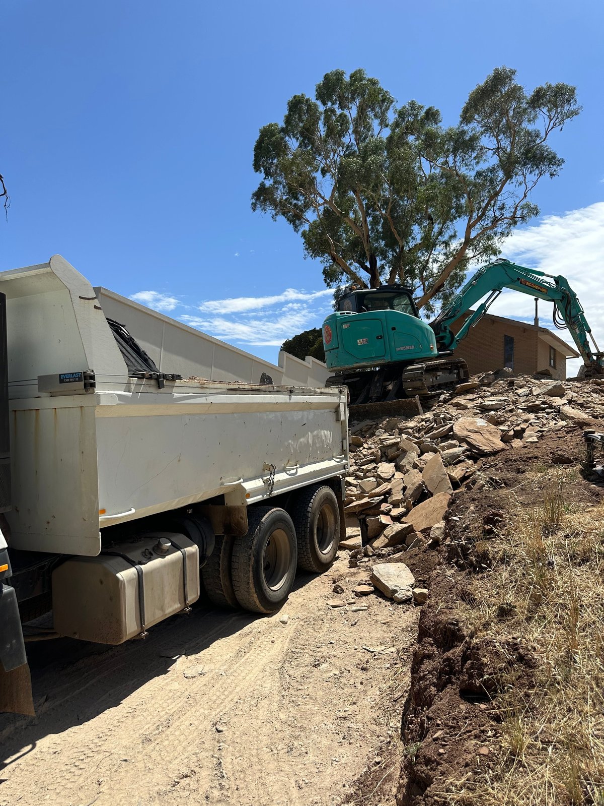 White dump truck and green excavator at construction site with piled rocks under clear blue sky