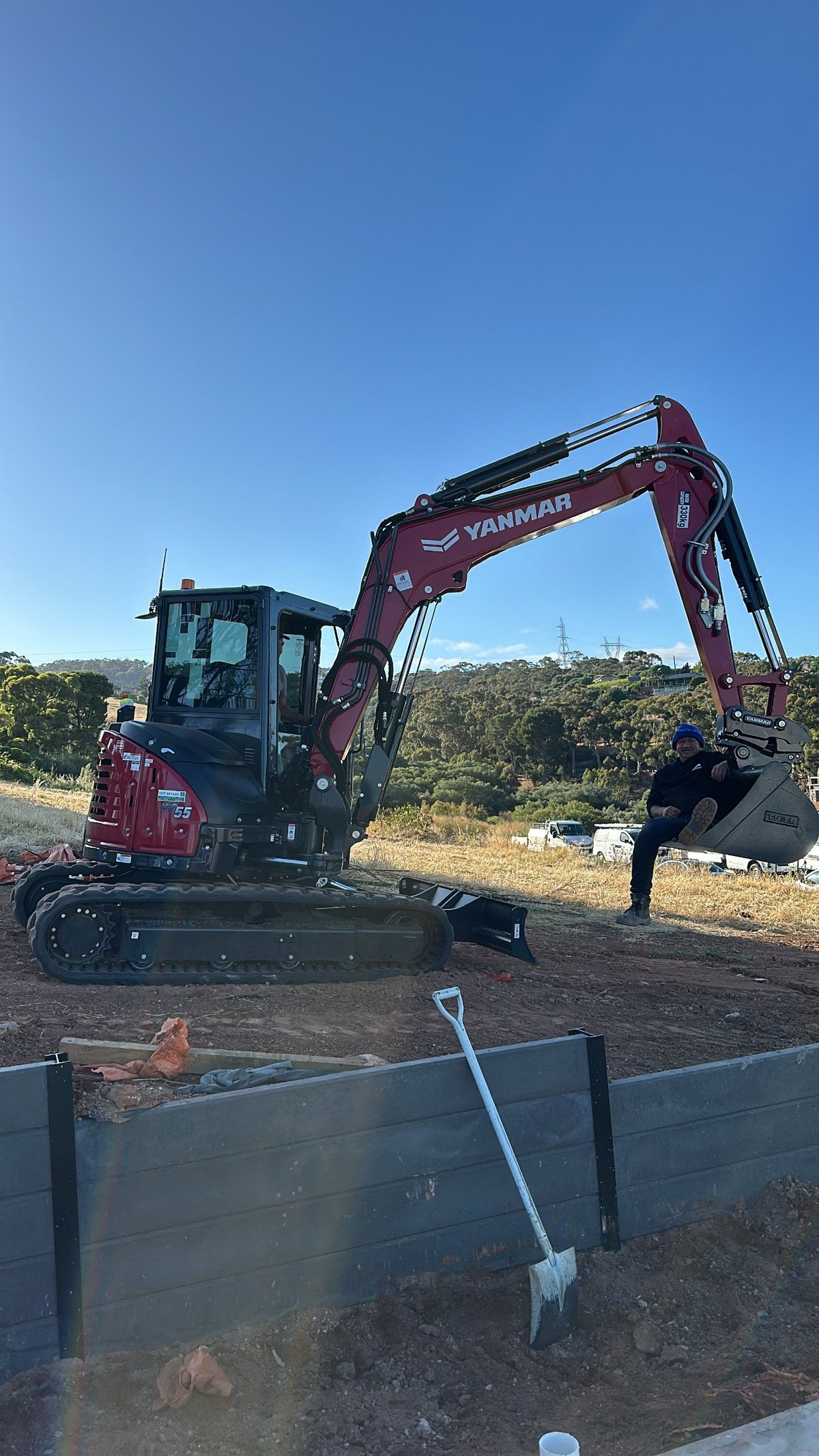 Red and black Yanmar excavator on a construction site with trees in the background under clear blue sky