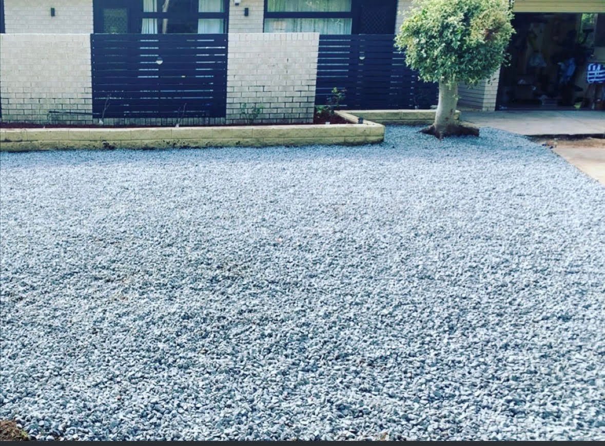 Gravel driveway in front of a brick building with navy blue gates and metal railings